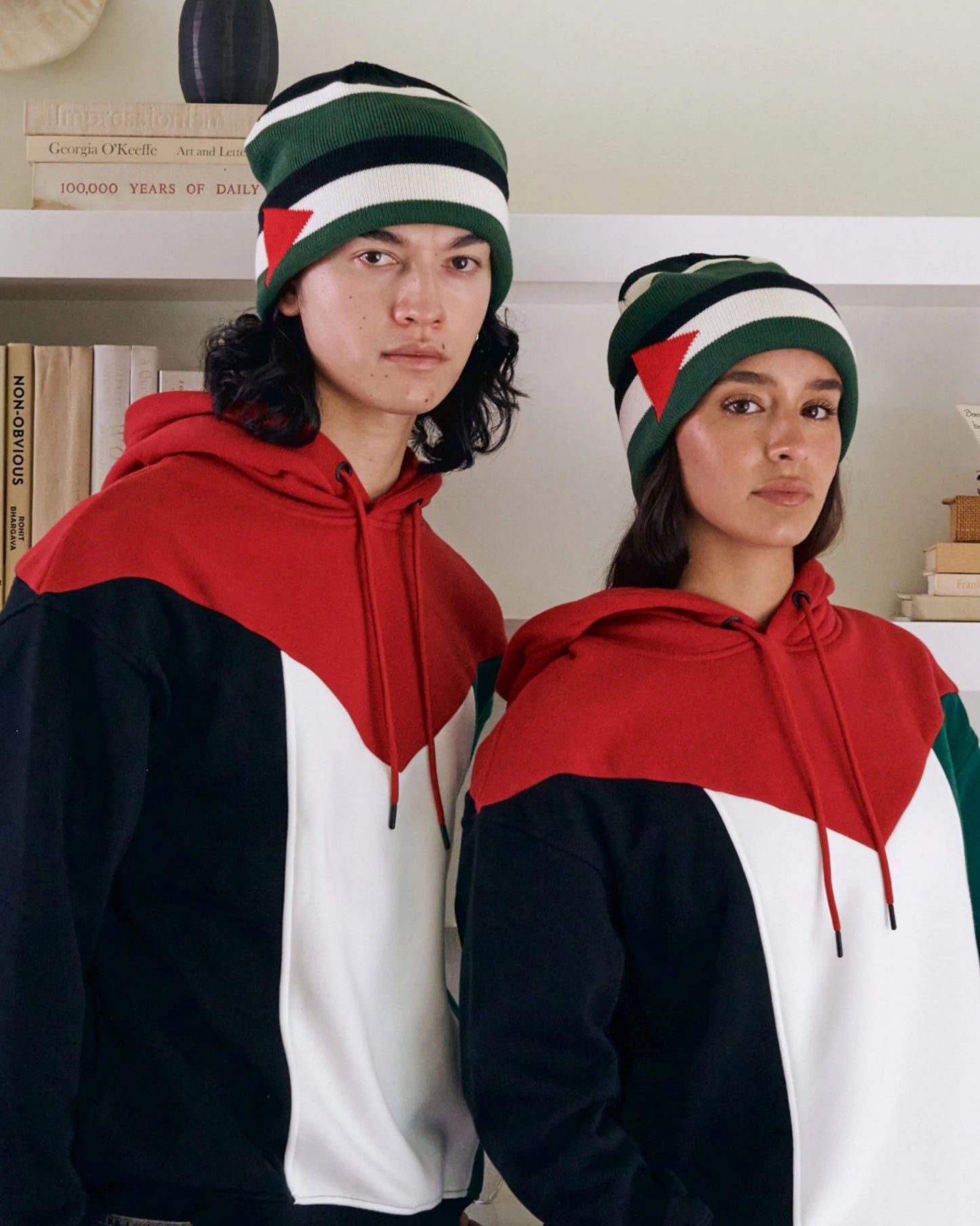 Two individuals wearing a Palestinian flag coloured matching hoodie and beanie, standing close together, facing the camera.
