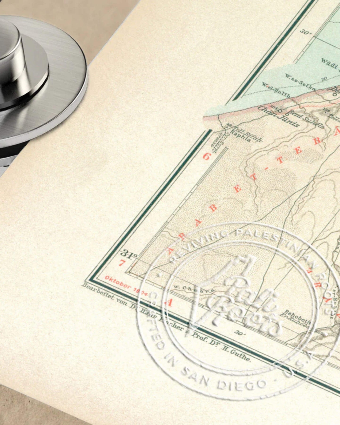 A partial view of a vintage map with a round embossed seal with PaliRoots logotype, and a metal object on the left, resting on a beige surface.