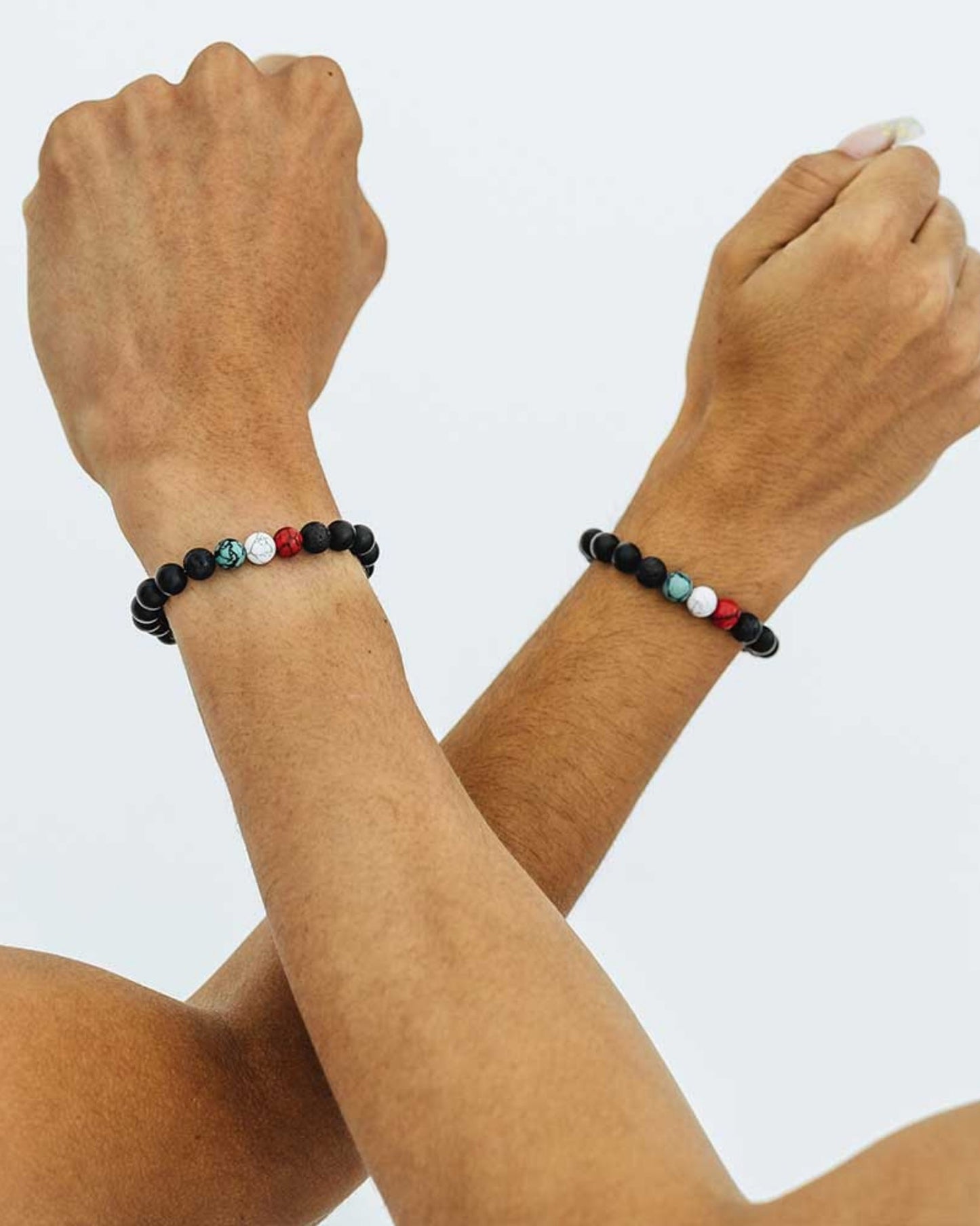 A close-up of two individuals holding hands, adorned with black, white, green and red beaded bracelets on each wrist.