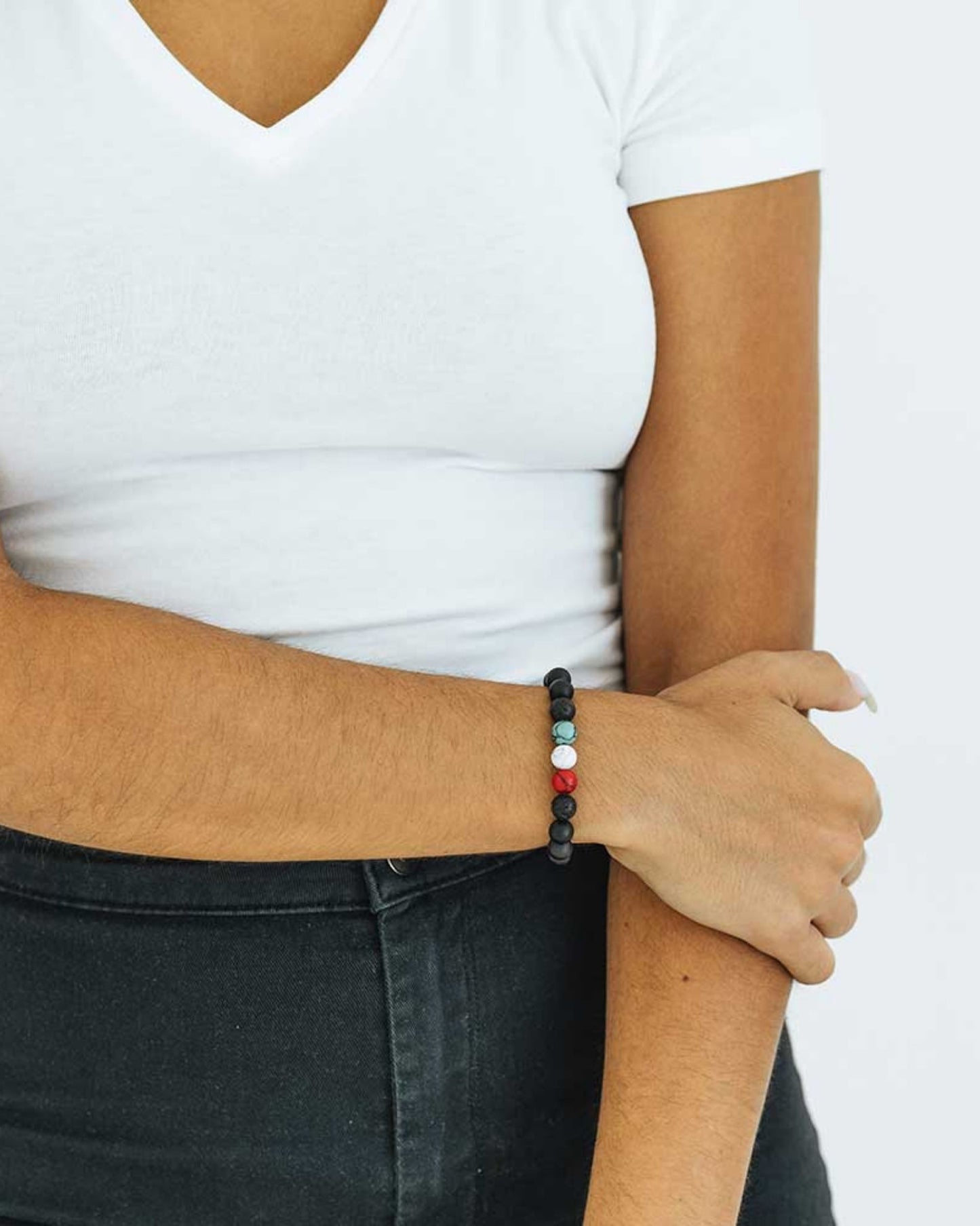 A woman in a casual outfit, wearing a black, white, green and red beaded bracelet on her right wrist.