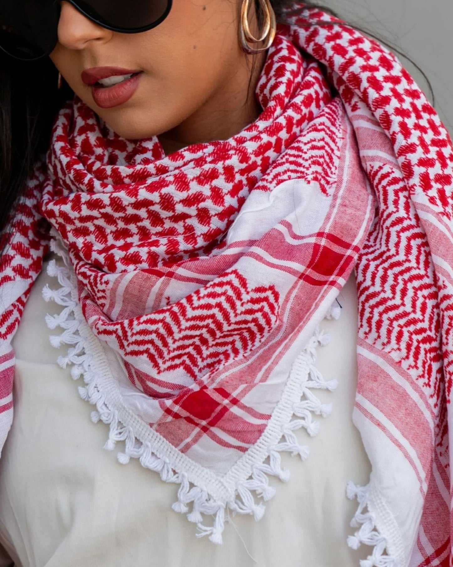 Close-up of a woman with sunglasses wearing a red and white Kufiya scarf around her neck.