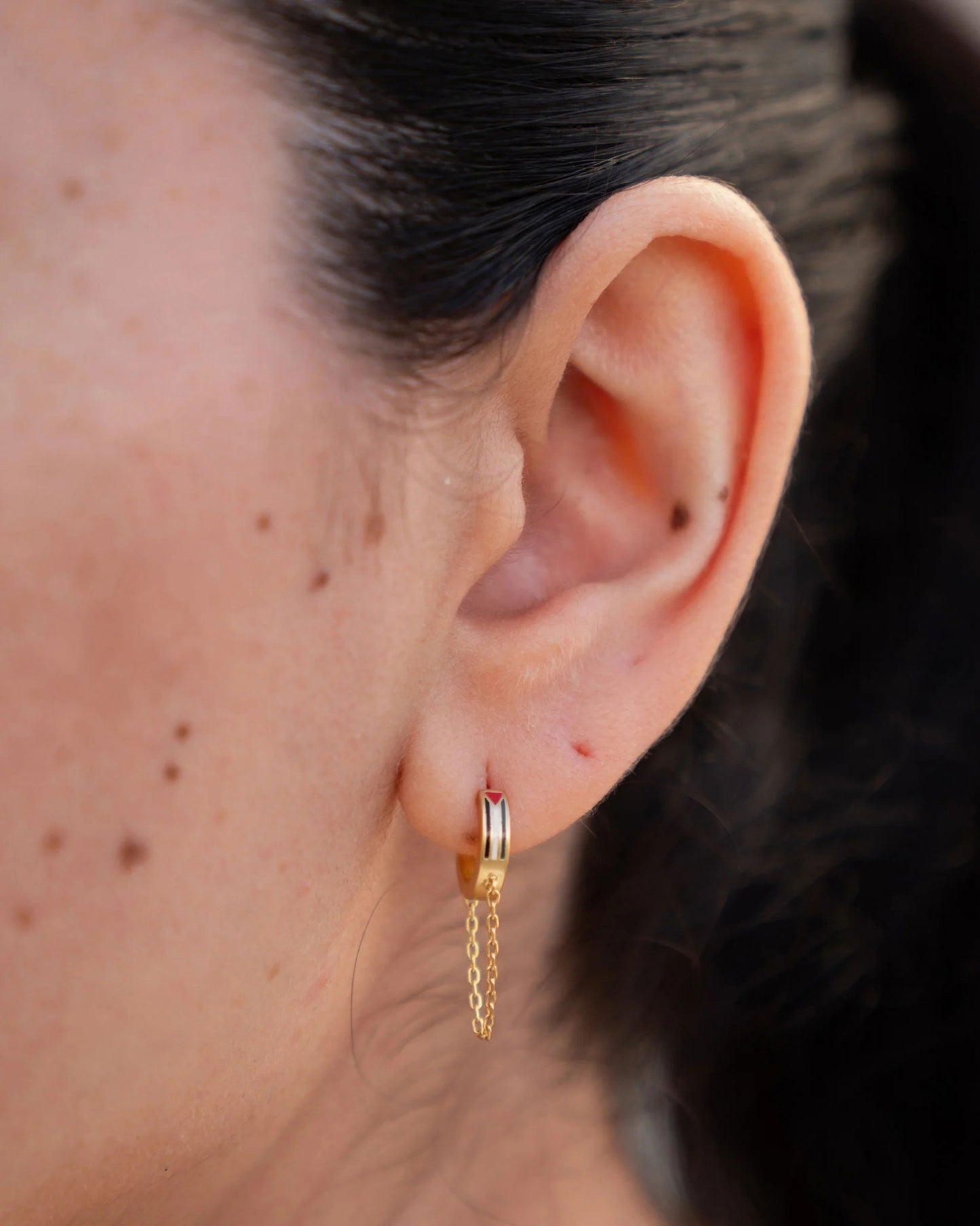 A close-up of a woman's face, displaying a gold earring with green and red details.