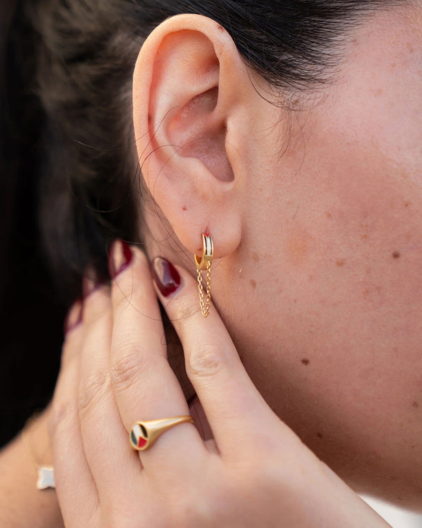 A woman wearing stylish gold earrings and a matching gold ring, with colourful details, highlighting her sophisticated accessories.